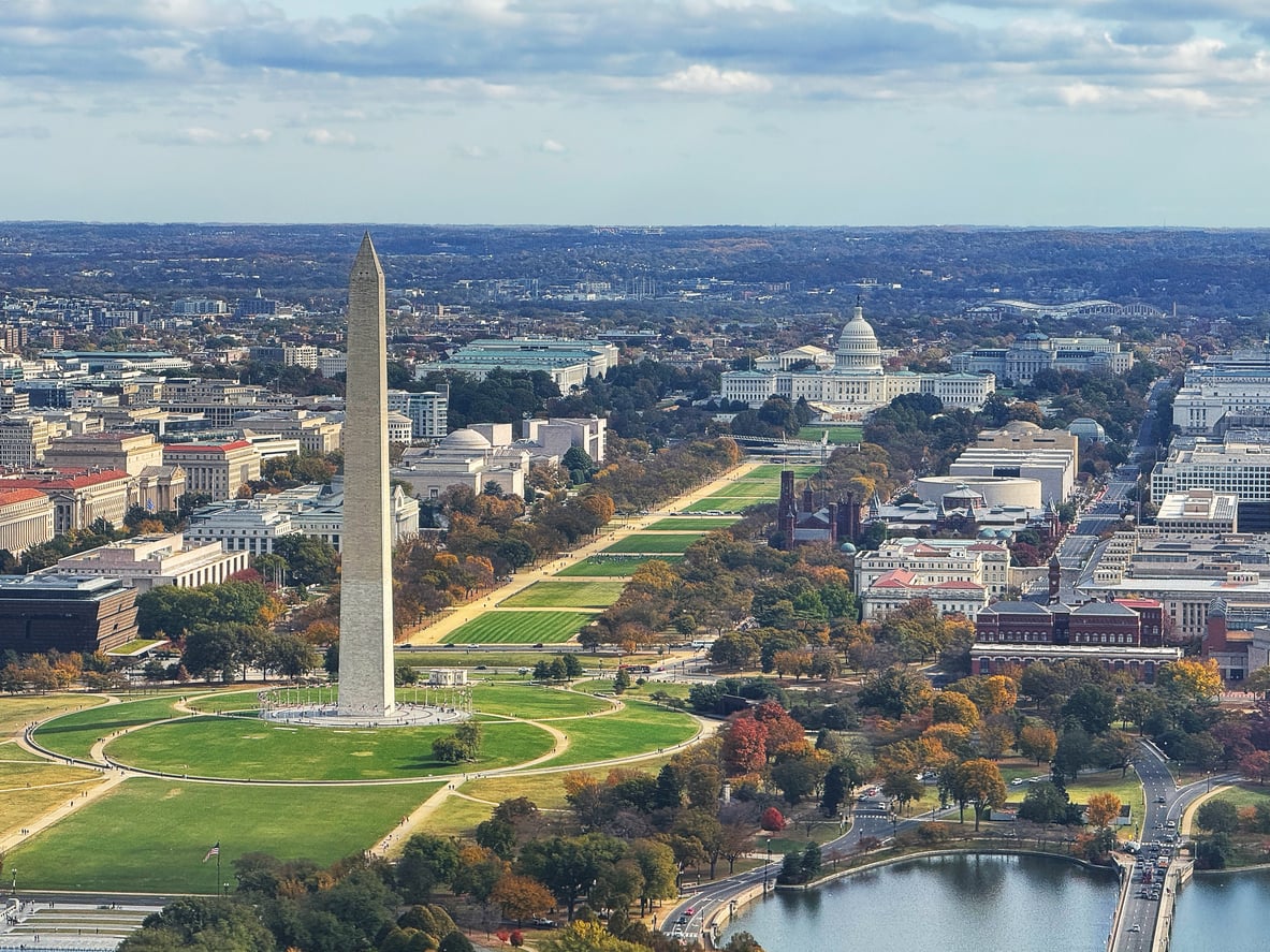 Aerial view of Washington, D.C., a vibrant East Coast city, featuring the Washington Monument in the foreground, the National Mall stretching towards the U.S. Capitol building in the distance, and the Tidal Basin in the bottom right corner on an autumn day.