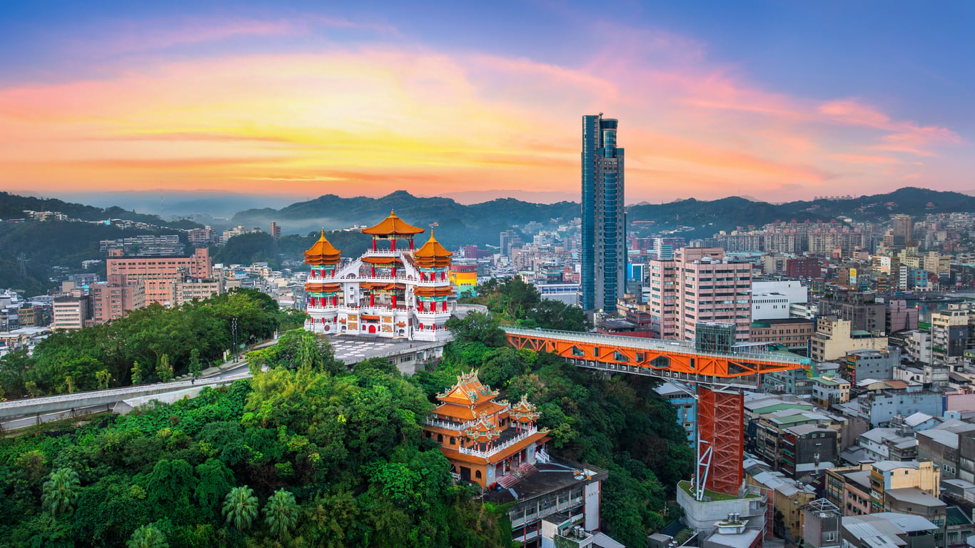 A cityscape at sunset with modern skyscrapers, traditional Chinese pagodas, lush green hills, and an orange elevated bridge crossing over buildings—this vibrant scene perfectly captures one of Asia’s most captivating travel destinations.