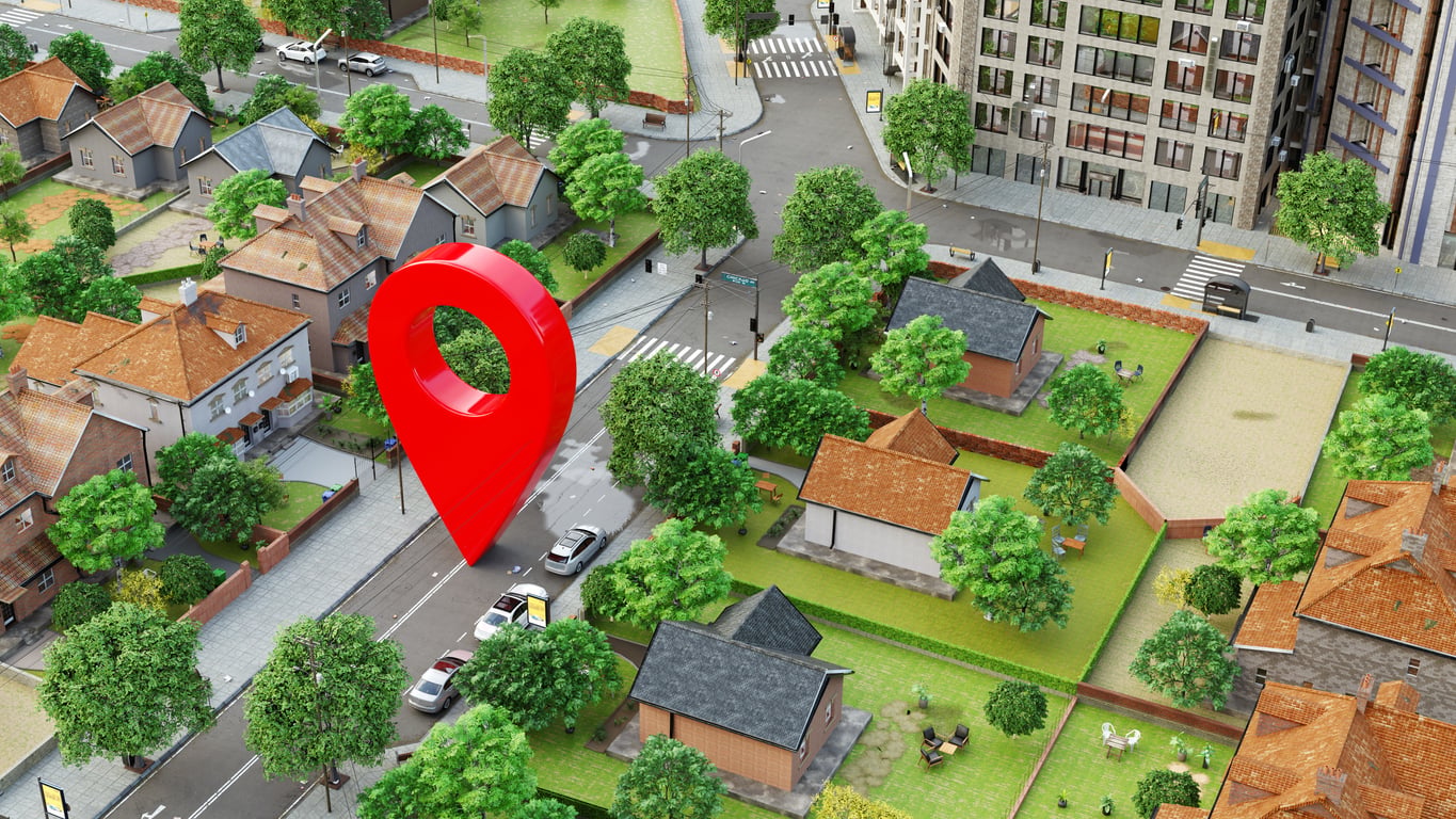 A 3D map shows a residential neighborhood with houses, trees, cars, and a large red location pin marking a spot on a street by several homes—perfect for those seeking hotel booking tips to find the ideal stay in nearby areas.