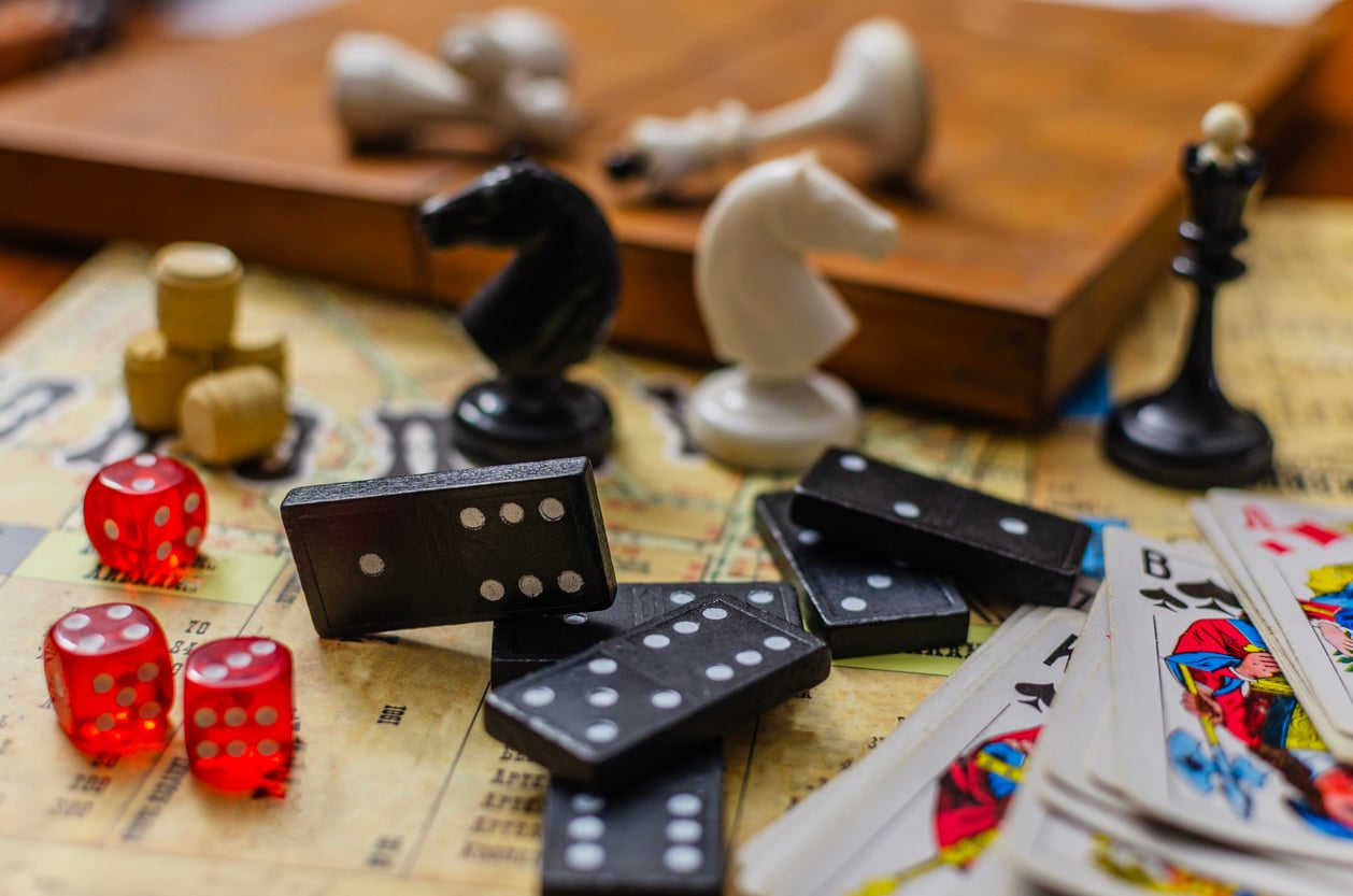 A close-up of various board game pieces, including dominoes, chess pieces, red dice, playing cards, and small wooden tokens spread over a vintage game board—perfect for those who appreciate the charm and strategy involved in expensive hobbies.