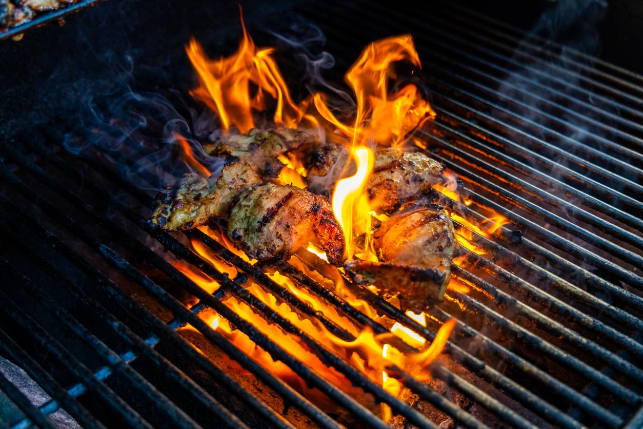Chicken pieces cooking on a grill with bright flames and smoke rising up around them, creating a sizzling and intense barbecue scene.