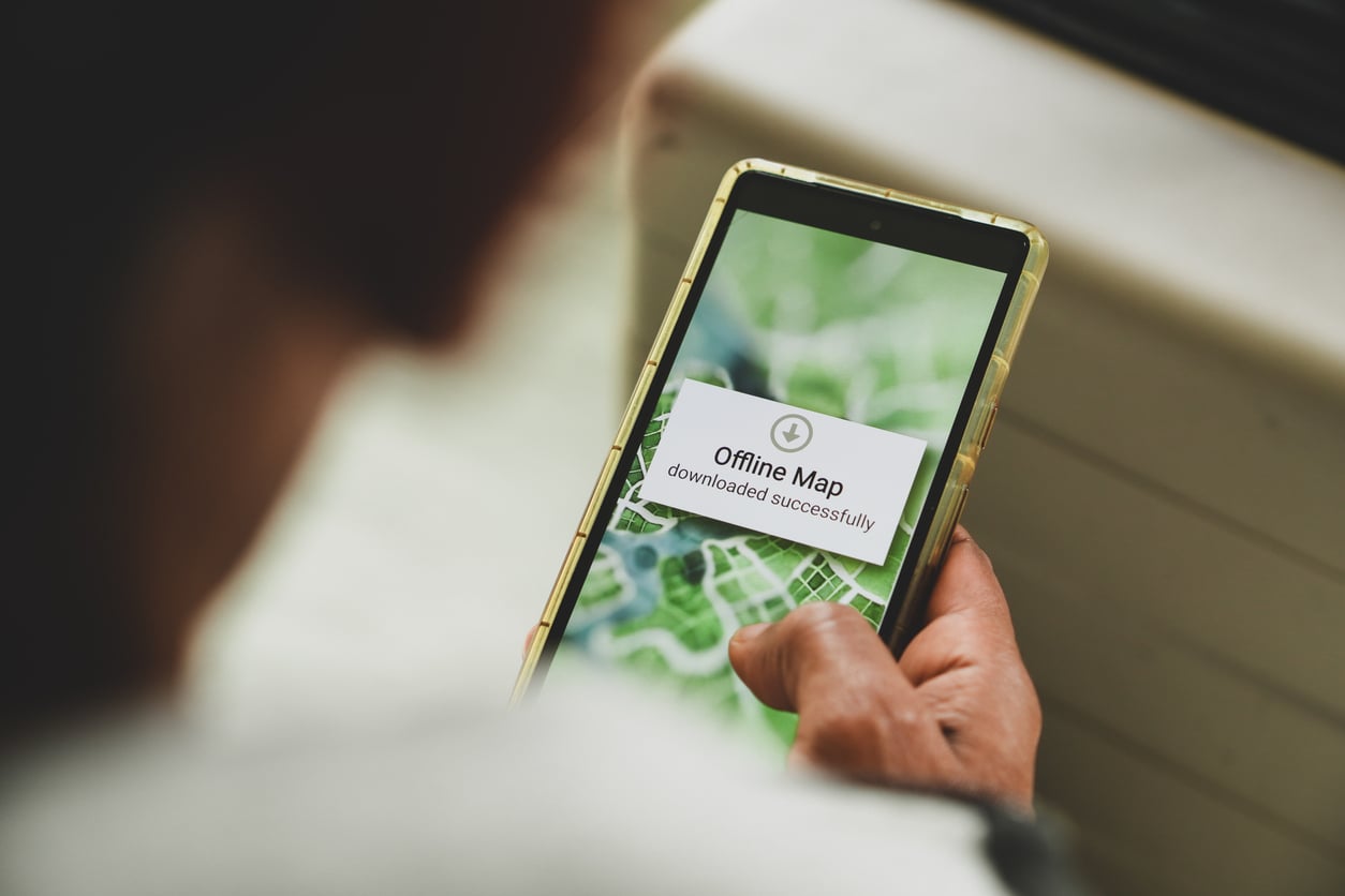A person holds a smartphone displaying a map with a notification that says, "Offline Map downloaded successfully," making it an essential item on any road trip checklist.
