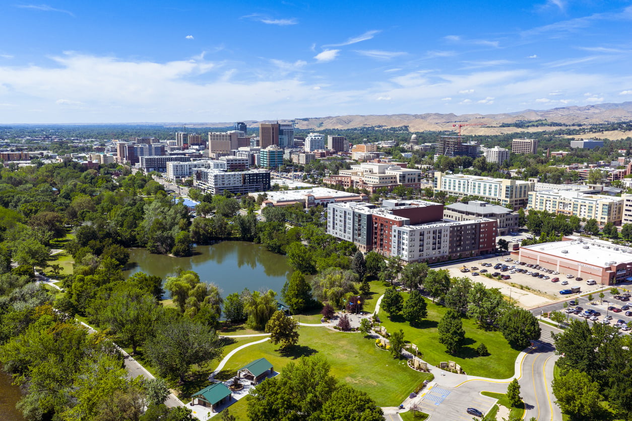Aerial view of a city with a mix of modern buildings, green parks, a pond, and surrounding trees under a blue sky with scattered clouds—an urban landscape that could easily be featured among the top 20 travel destinations for its unique blend of nature and architecture.