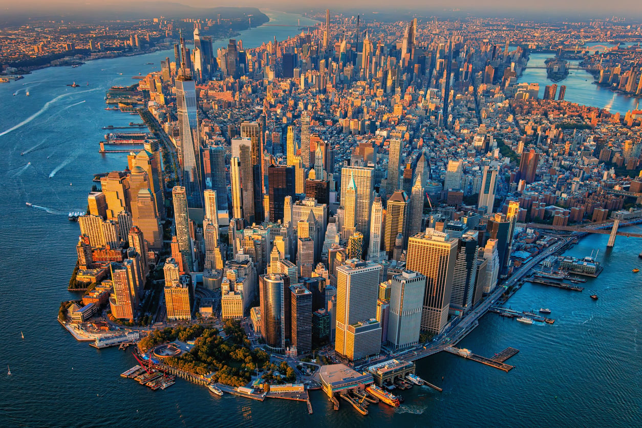 Aerial view of Lower Manhattan with travel-friendly skyscrapers, rivers on both sides, and the city stretching into the distance at sunset.