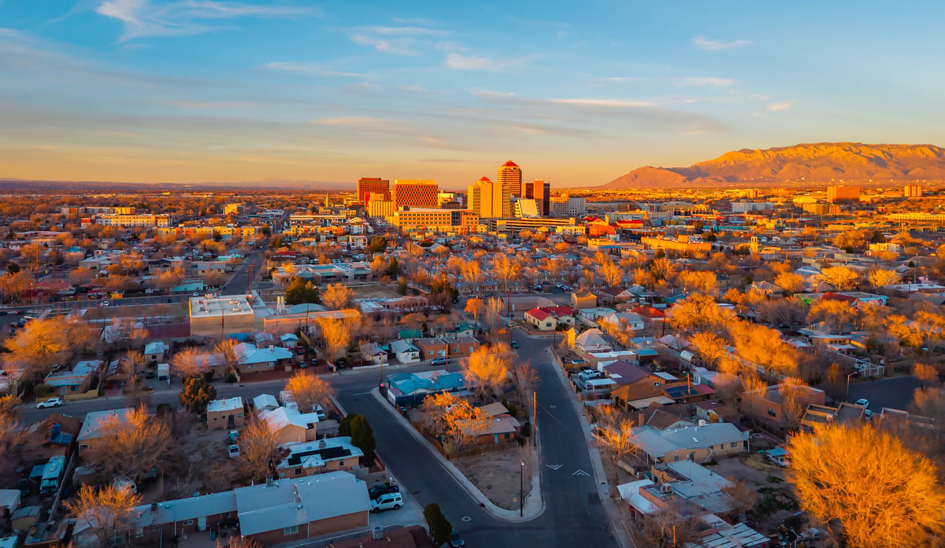 Aerial view of a city at sunset, with residential houses in the foreground and tall buildings in the background, mountains visible on the right under a mostly clear sky—an inviting glimpse of one of the world’s stunning urban destinations.
