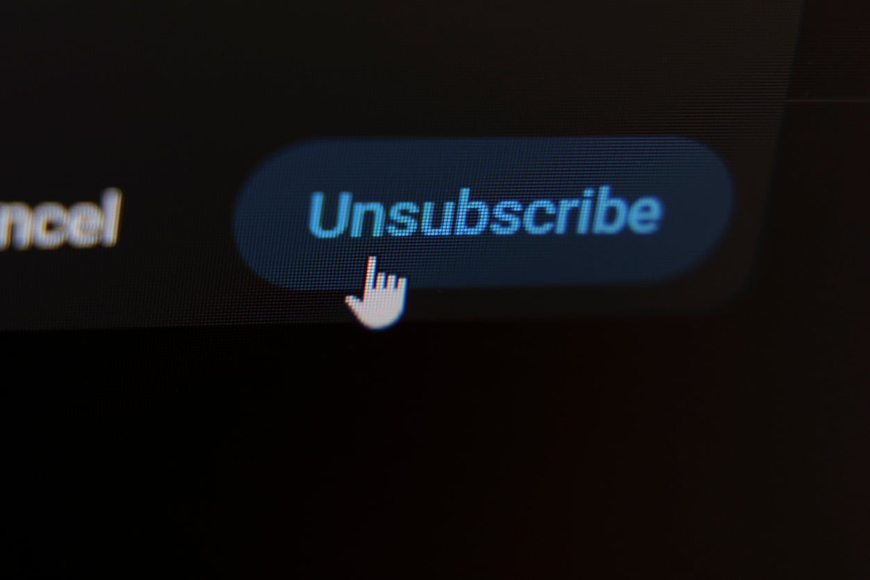 A computer screen shows a cursor hand icon hovering over a blue "Unsubscribe" button, indicating an option to opt out or stop receiving emails or notifications.
