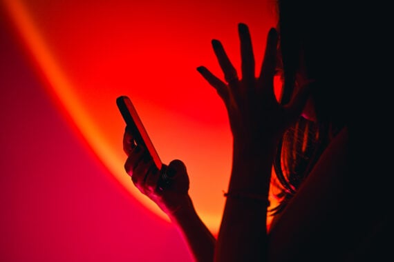 A person holding a smartphone raises a hand in frustration or surprise, silhouetted against a dramatic red and orange light background&mdash;a striking contrast to life before smartphones.