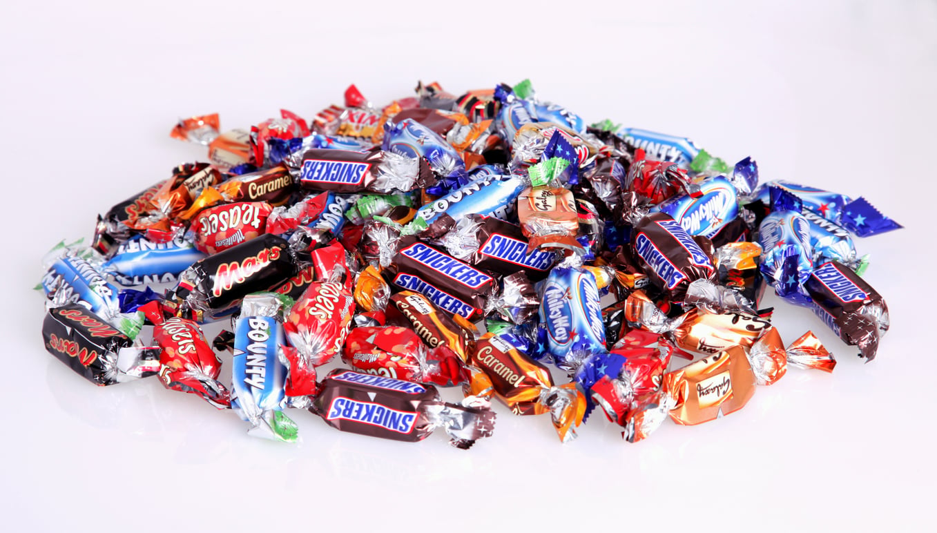 A pile of assorted wrapped candies, including brands like Snickers, Mars, Bounty, and Twix, displayed on a white surface.