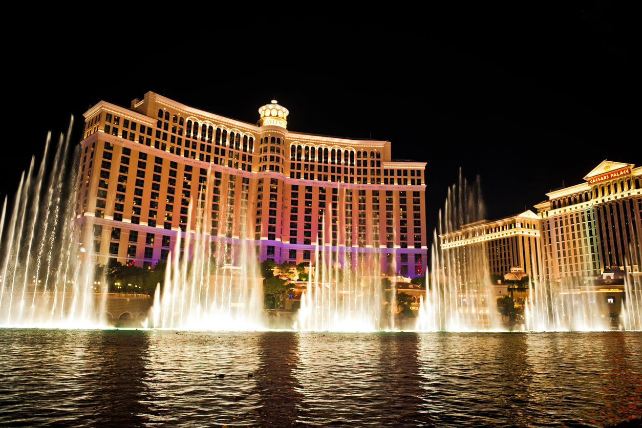 Bellagio Hotel in Las Vegas at night, illuminated with water fountains in front, spraying high into the air, reflecting lights on the water.