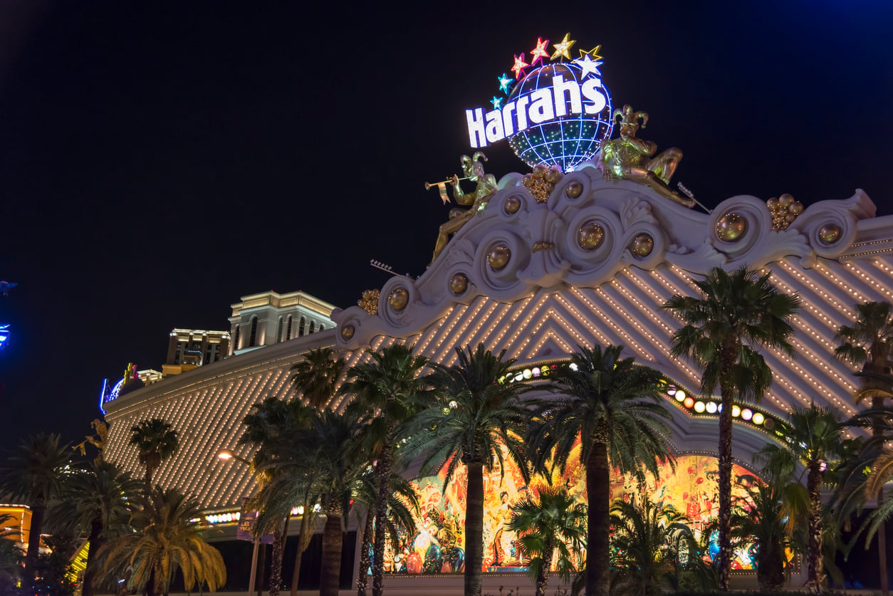 Harrah’s Las Vegas casino at night, brightly lit with neon lights, palm trees in front, and a decorative sign featuring stars and gold statues on the roof.