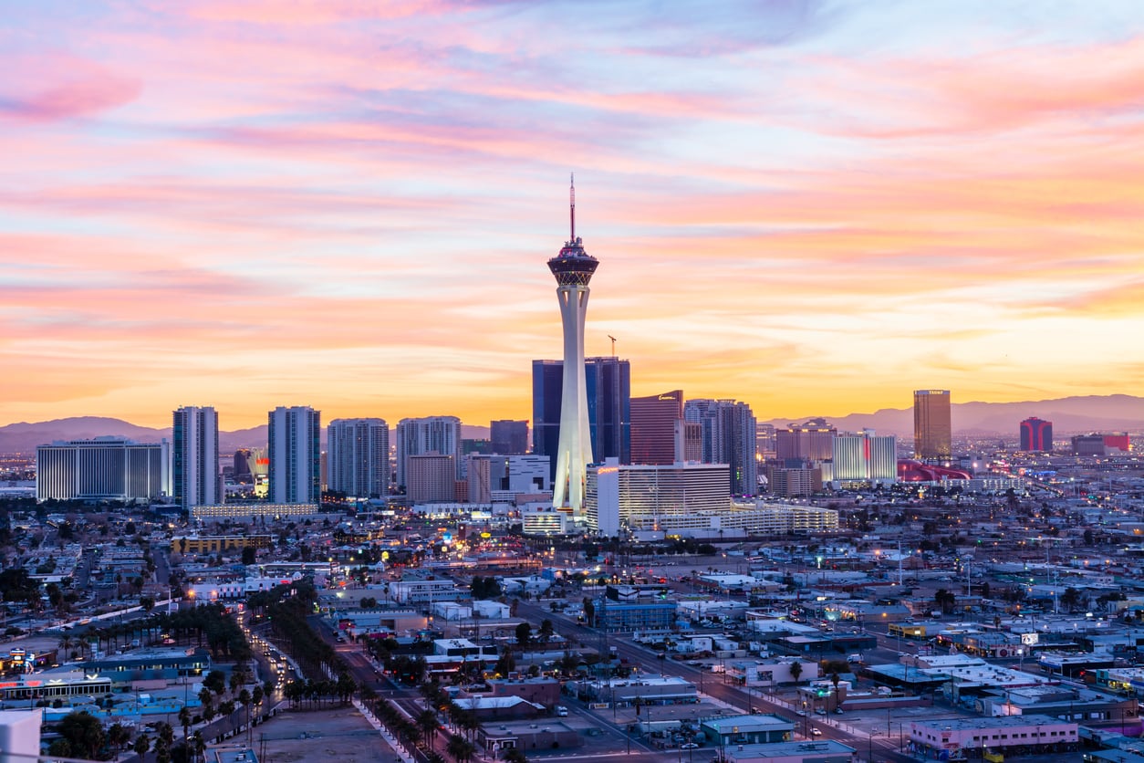 Las Vegas city skyline at sunset, featuring the Stratosphere Tower surrounded by buildings and colorful clouds in the sky.