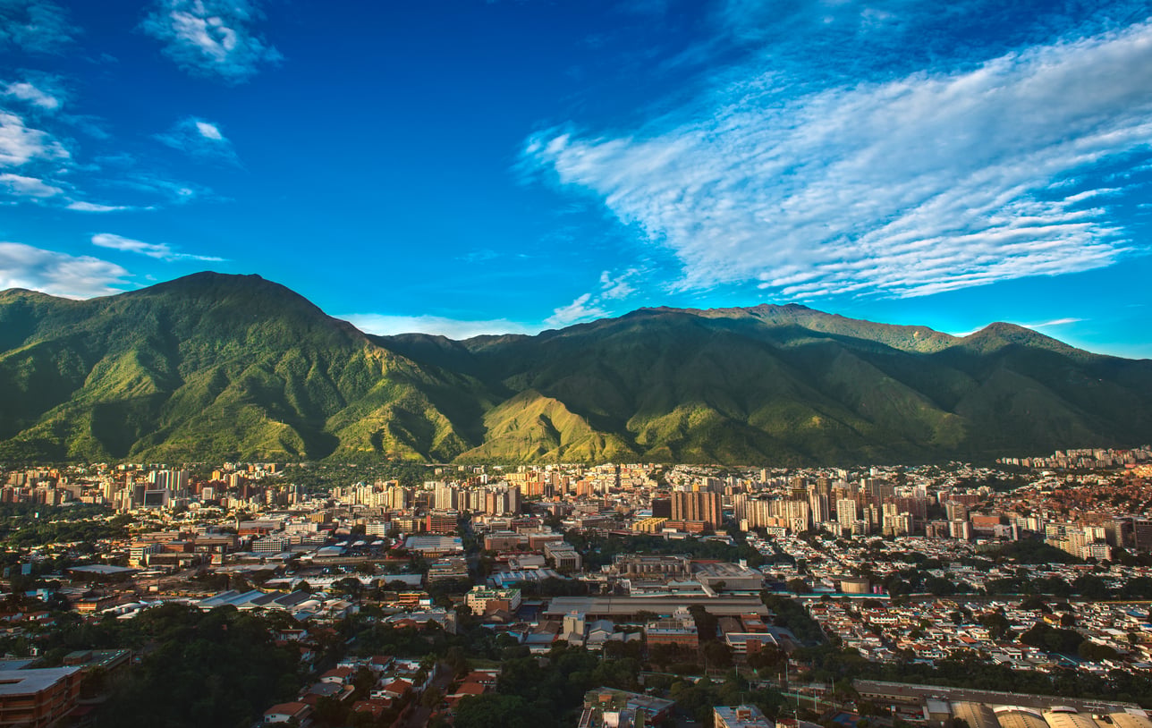 Cityscape with tall buildings in the foreground, lush green mountains in the background, and a blue sky with wispy clouds overhead—a captivating scene that highlights one of the world’s most vibrant travel destinations.
