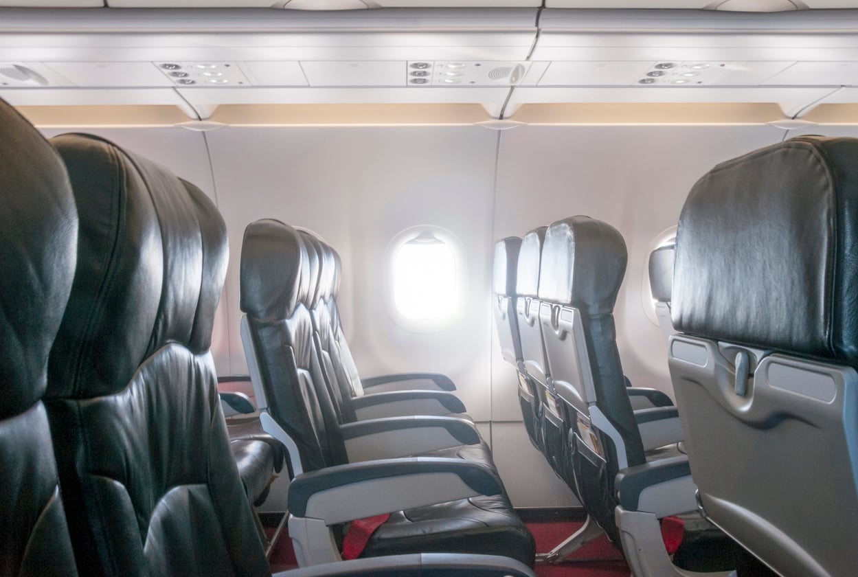 Empty airplane seats in a row next to a window with sunlight streaming in, showing a clean and modern aircraft interior.