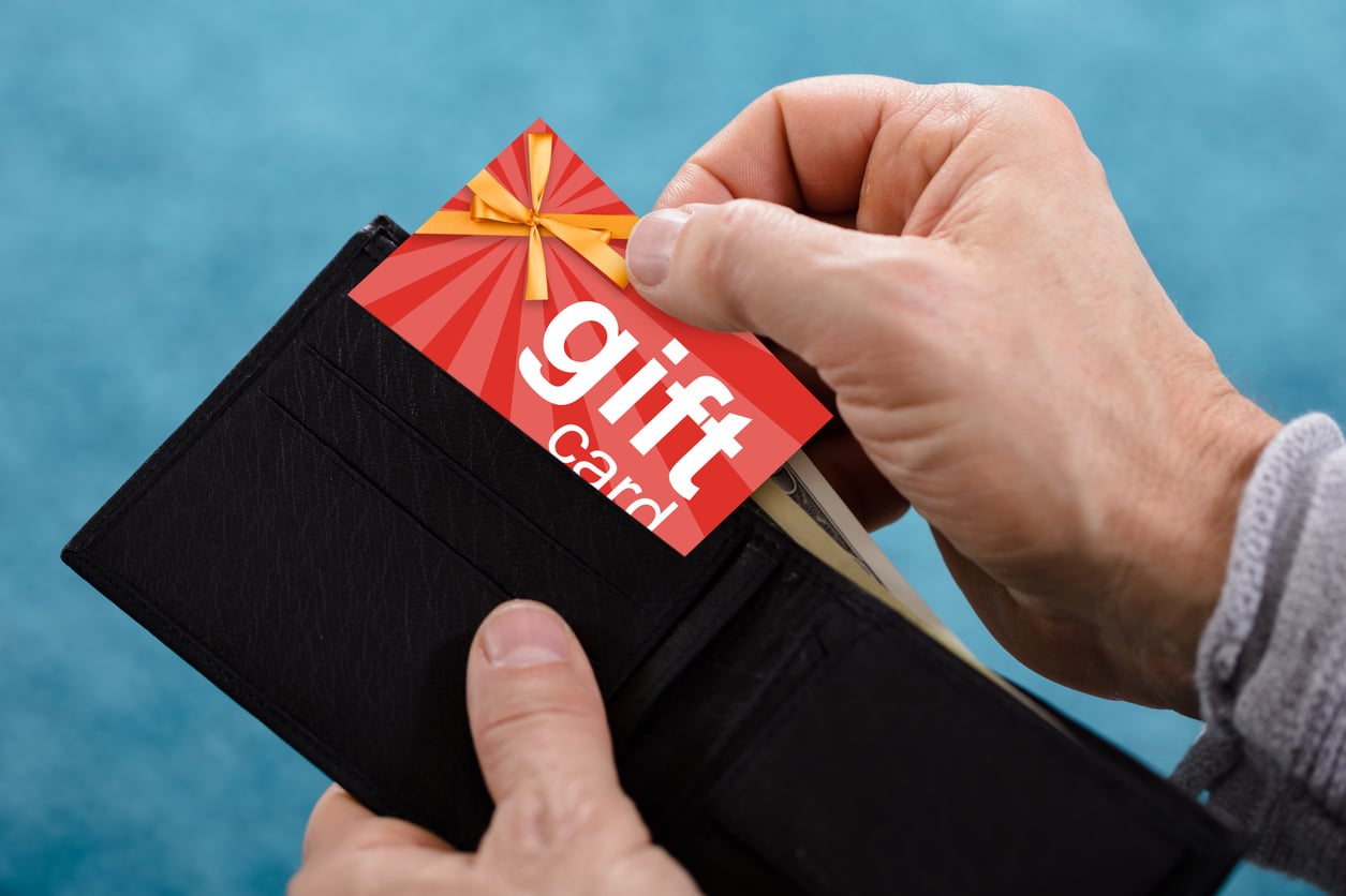 A person pulls a colorful gift card with a ribbon design from a black wallet, against a blue background—perfect for anyone looking to try out new movie theater hacks.