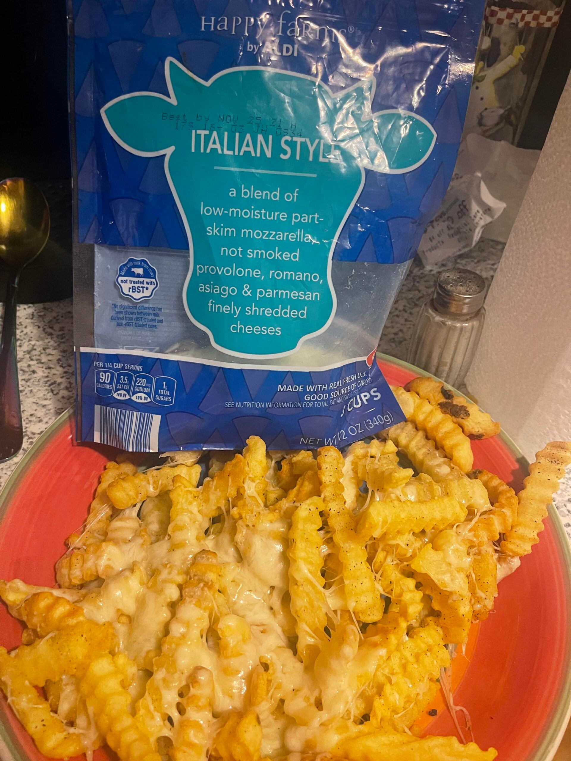 Crinkle-cut fries on a plate topped with the best shredded cheese, melted to perfection, with a bag of Happy Farms Italian Style shredded cheese in the background.