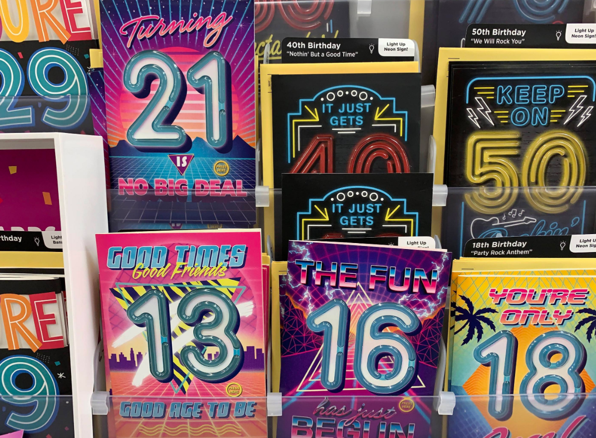 A display of colorful birthday cards at Walmart features bold numbers for ages 13, 16, 21, 29, 40, and 50 with fun phrases like “No Big Deal” and “Good Times Good Friends”—all neatly arranged in a store rack.