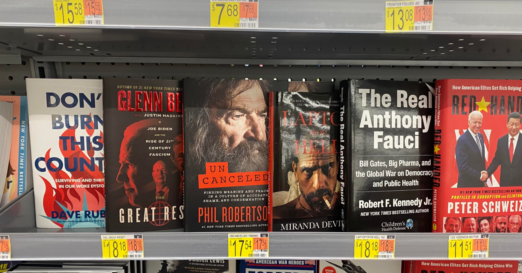 A Walmart bookstore shelf displays five political books by various authors with colorful covers, including titles by Dave Rubin, Glenn Beck, Phil Robertson, Miranda Devine, and Robert F. Kennedy Jr. Price tags are visible below each book.