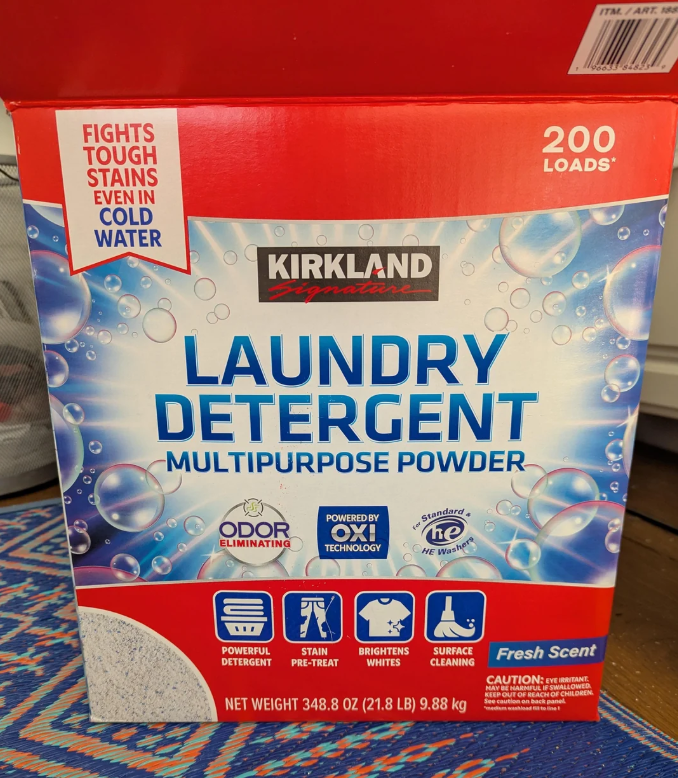 A box of Kirkland Signature Laundry Detergent Multipurpose Powder, labeled for 200 loads, featuring claims like odor elimination, stain fighting, and whitening. The box is mostly red and blue with bubbles and text.