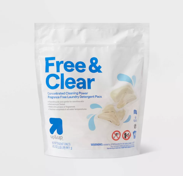 A white resealable pouch labeled "Free & Clear" contains fragrance-free laundry detergent pods. The packaging features blue text, images of detergent pods, and icons indicating safety warnings and sensitive skin compatibility.