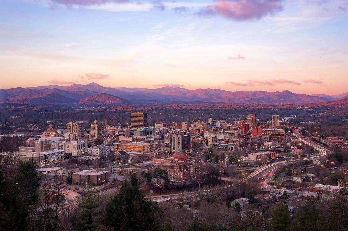 A cityscape at sunset with a cluster of buildings in the foreground and mountains in the background under a partly cloudy sky, reminiscent of the charm found in popular tourist towns.