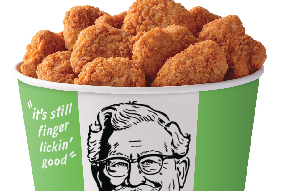 A green and white KFC bucket filled with crispy fried chicken nuggets. The bucket features the KFC logo with a smiling Colonel Sanders and the slogan, "it's still finger lickin' good.