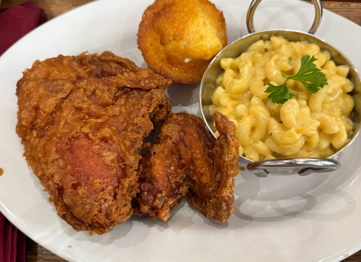 A plate with fried chicken, a muffin, and a small metal dish of macaroni and cheese garnished with parsley.