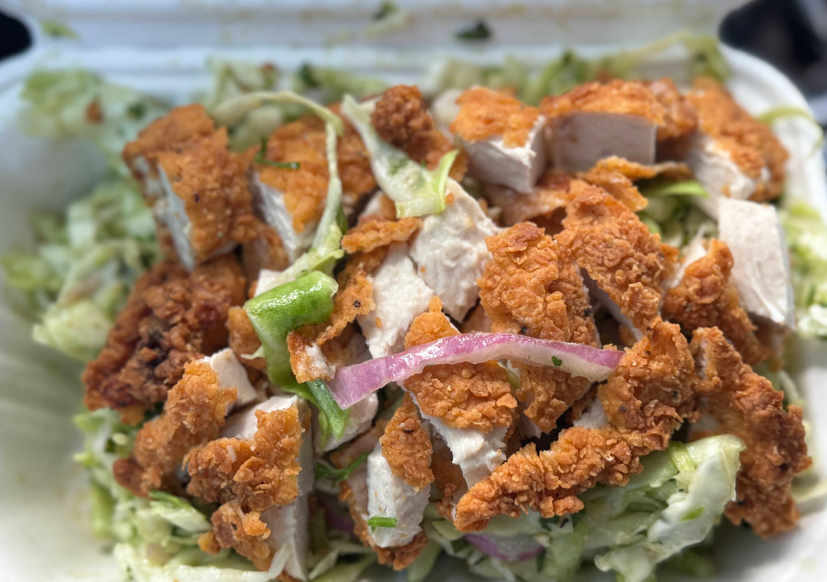 Crispy fried chicken pieces on top of a bed of shredded lettuce, green bell peppers, and red onions, served in a takeout container.