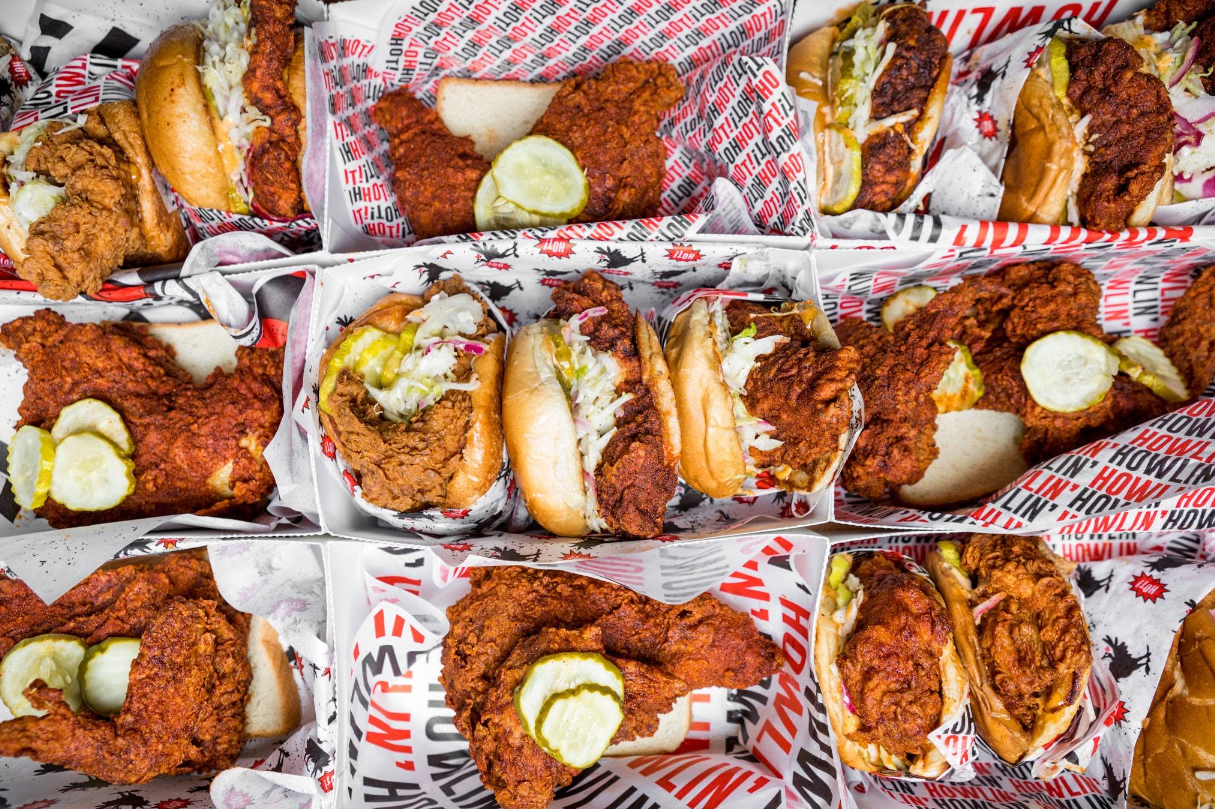 A variety of spicy fried chicken sandwiches and tenders, topped with pickles and coleslaw, served in paper trays with branded liners.