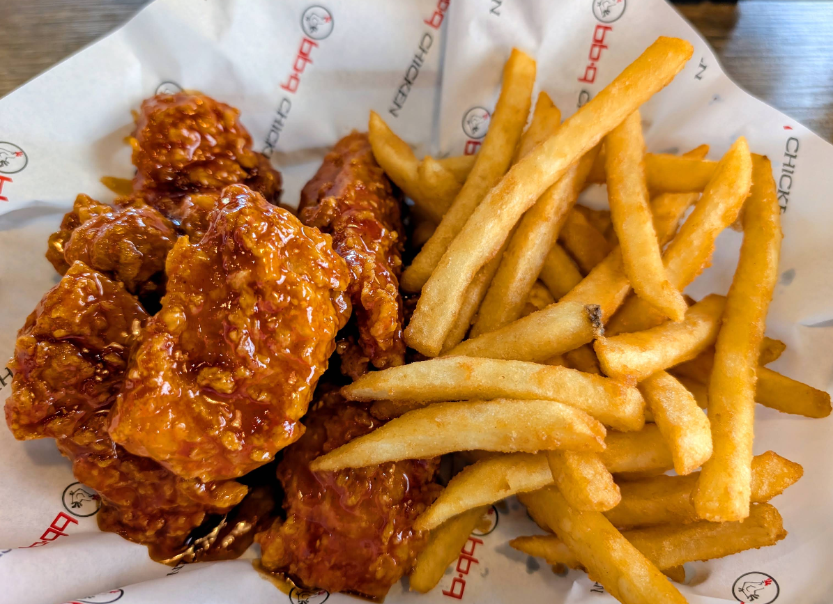 A basket of golden French fries and crispy fried chicken wings—served by one of the fastest-growing fried chicken chains—coated in a shiny, reddish-brown sauce and presented on white branded paper.
