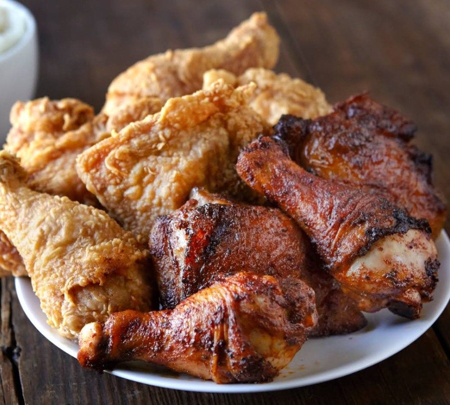 A plate filled with golden fried chicken and dark, crispy roasted chicken drumsticks from one of the fastest-growing fried chicken chains sits on a wooden table.