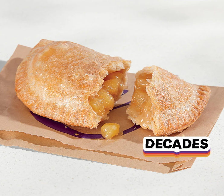 A golden-brown fried pie filled with gooey apple chunks sits on a brown paper wrapper; the word "DECADES" appears in a retro font at the edge.