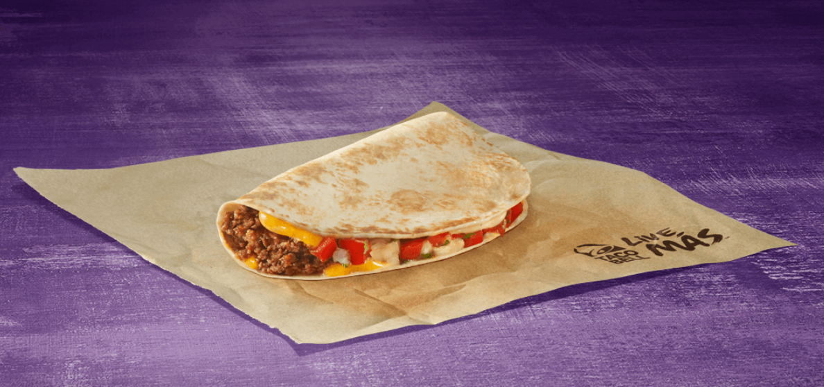 A folded tortilla filled with ground beef, melted cheese, and diced tomatoes sits on a brown wrapper with Taco Bell’s logo, against a purple background.
