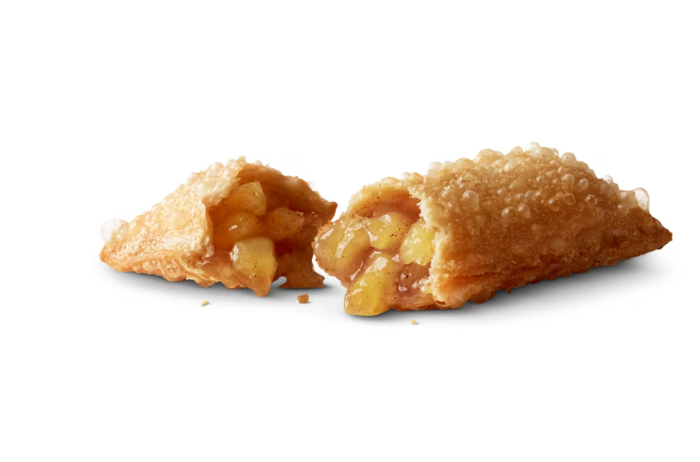 A golden-brown fried pastry filled with warm apple chunks and cinnamon, cut in half to show the gooey filling, against a white background.