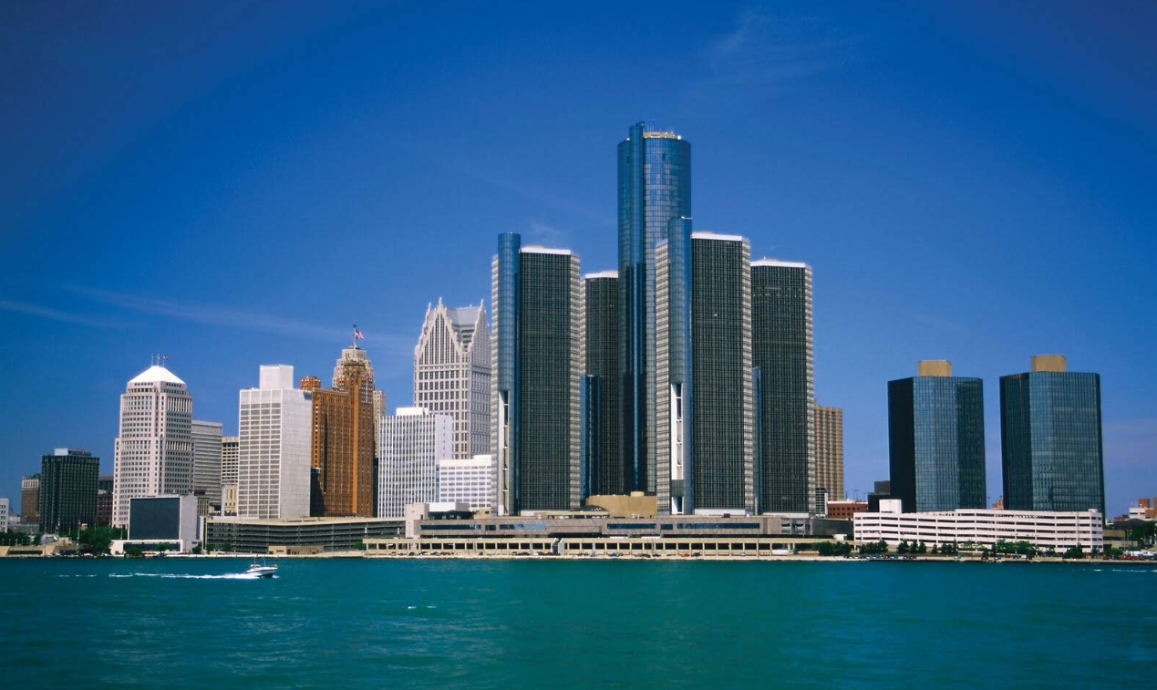 Detroit skyline with modern and historic skyscrapers under a clear blue sky, viewed from across the river with water in the foreground—a striking scene that highlights why Detroit has become one of the Midwest’s must-see destinations.