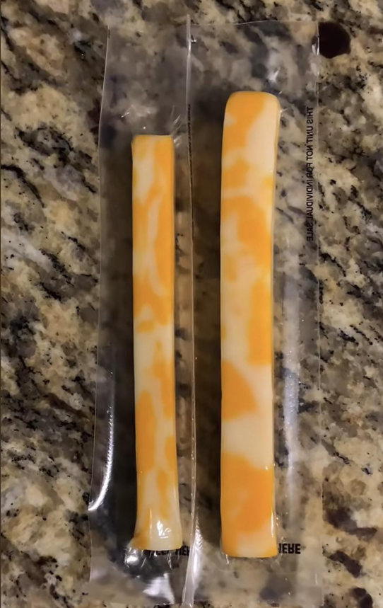 Two unopened marbled Colby Jack cheese sticks of noticeably different thickness and length rest on a granite countertop.