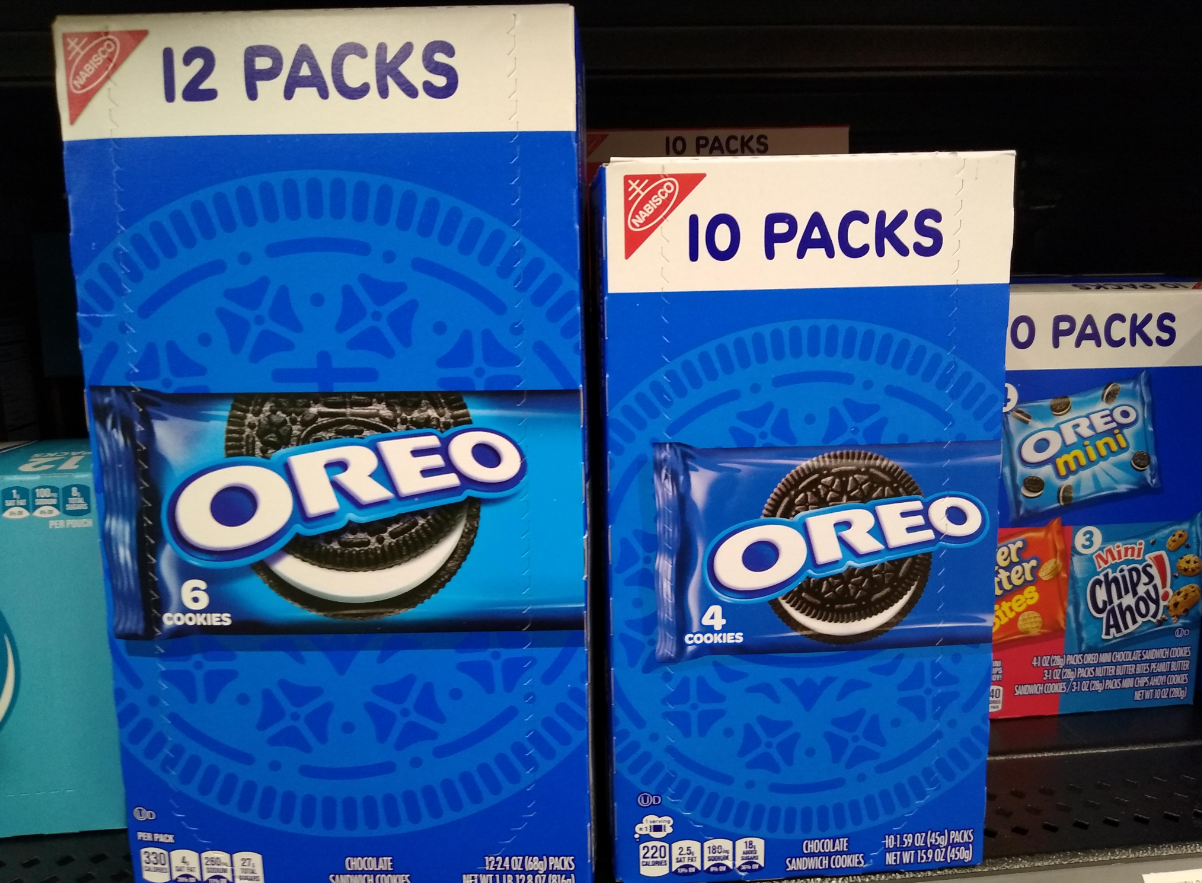 Two blue boxes of Oreo cookies on a store shelf, one labeled “12 packs” with 6 cookies per pack, and the other “10 packs” with 4 cookies per pack. Oreo branding and cookie images are visible on both boxes.