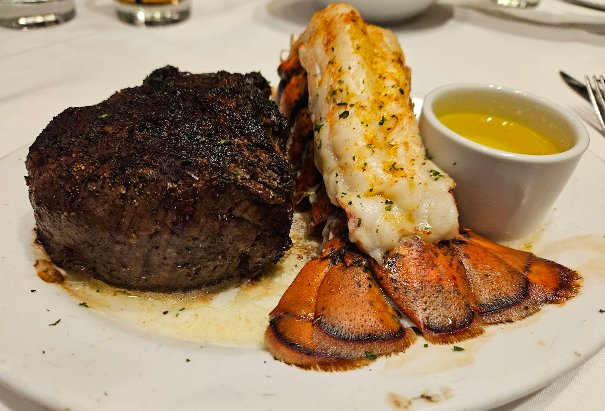 A plate with a grilled filet mignon, a broiled lobster tail, and a small cup of melted butter on the side evokes luxury far beyond a cheap all you can eat breakfast, served elegantly on a white tablecloth.