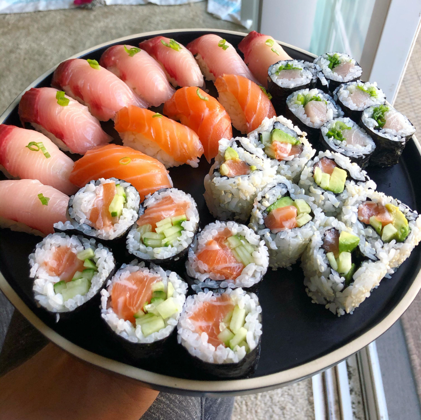A black plate with assorted sushi rolls and nigiri, including salmon, tuna, and cucumber-filled maki rolls, arranged in a circular pattern.