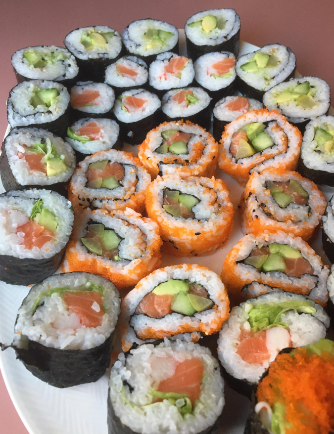 A plate of assorted sushi rolls, including ones wrapped in seaweed, some in orange roe, filled with rice, avocado, cucumber, and fish, arranged neatly on a white plate.