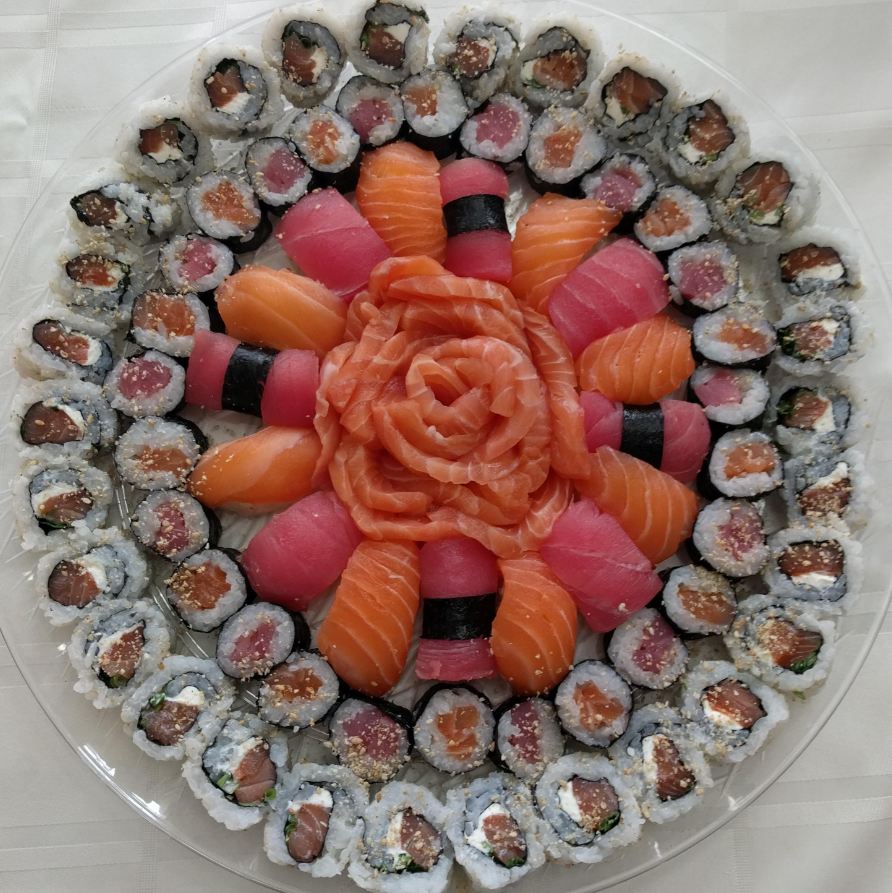 A large platter of assorted sushi rolls and nigiri, arranged in concentric circles with sliced salmon in a rose shape at the center, surrounded by rolls and pieces of tuna and salmon nigiri.