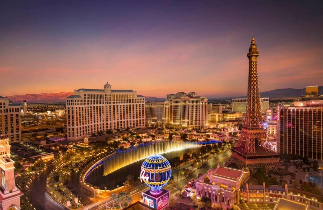 Las Vegas Strip at sunset, featuring illuminated hotels, the Bellagio fountain, and a replica of the Eiffel Tower with colorful lights against a vibrant sky—one of the most iconic travel destinations in the world.
