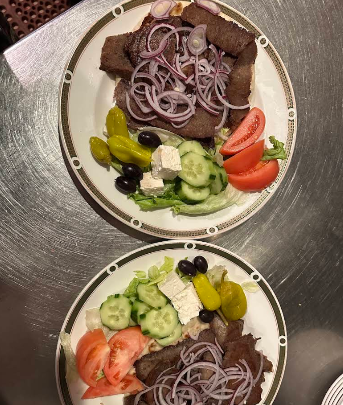 Two plates of Greek salad with sliced tomatoes, cucumbers, feta cheese, olives, pepperoncini, lettuce, and gyro meat topped with red onions, arranged on a metallic surface—perfect before a cheap all you can eat breakfast.