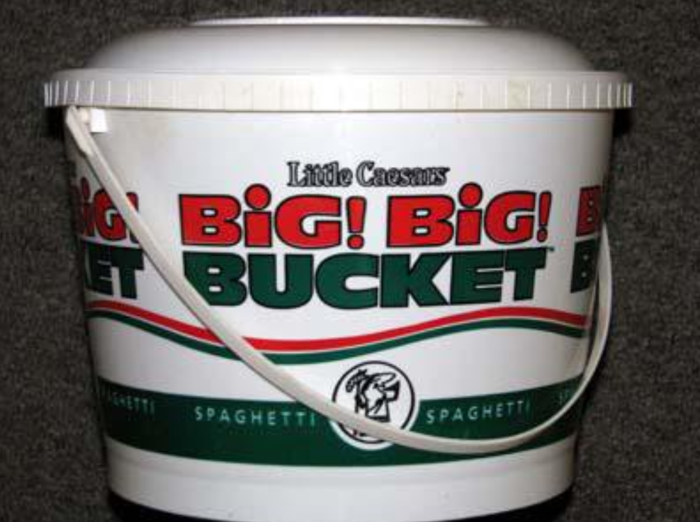 A large white plastic bucket labeled "Little Caesars BIG! BIG! BUCKET Spaghetti" with a handle, sitting against a dark background.