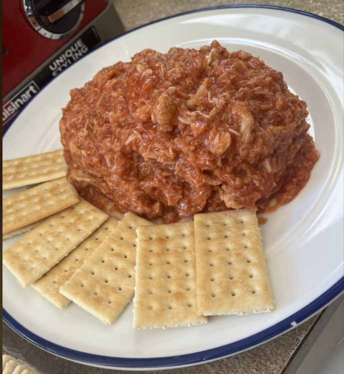 A plate with a mound of shredded, reddish tuna salad or dip, surrounded by several rectangular saltine crackers.