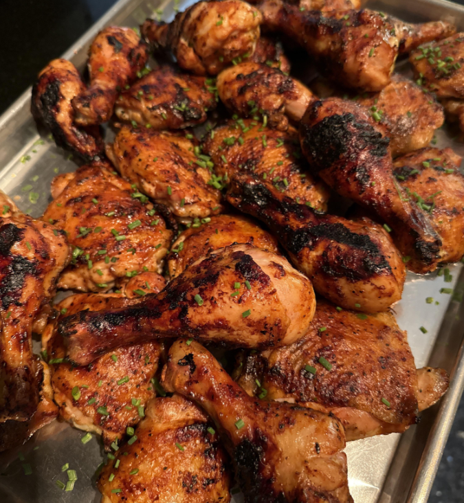A tray of grilled chicken drumsticks and thighs, seasoned and garnished with chopped herbs, showing charred grill marks.