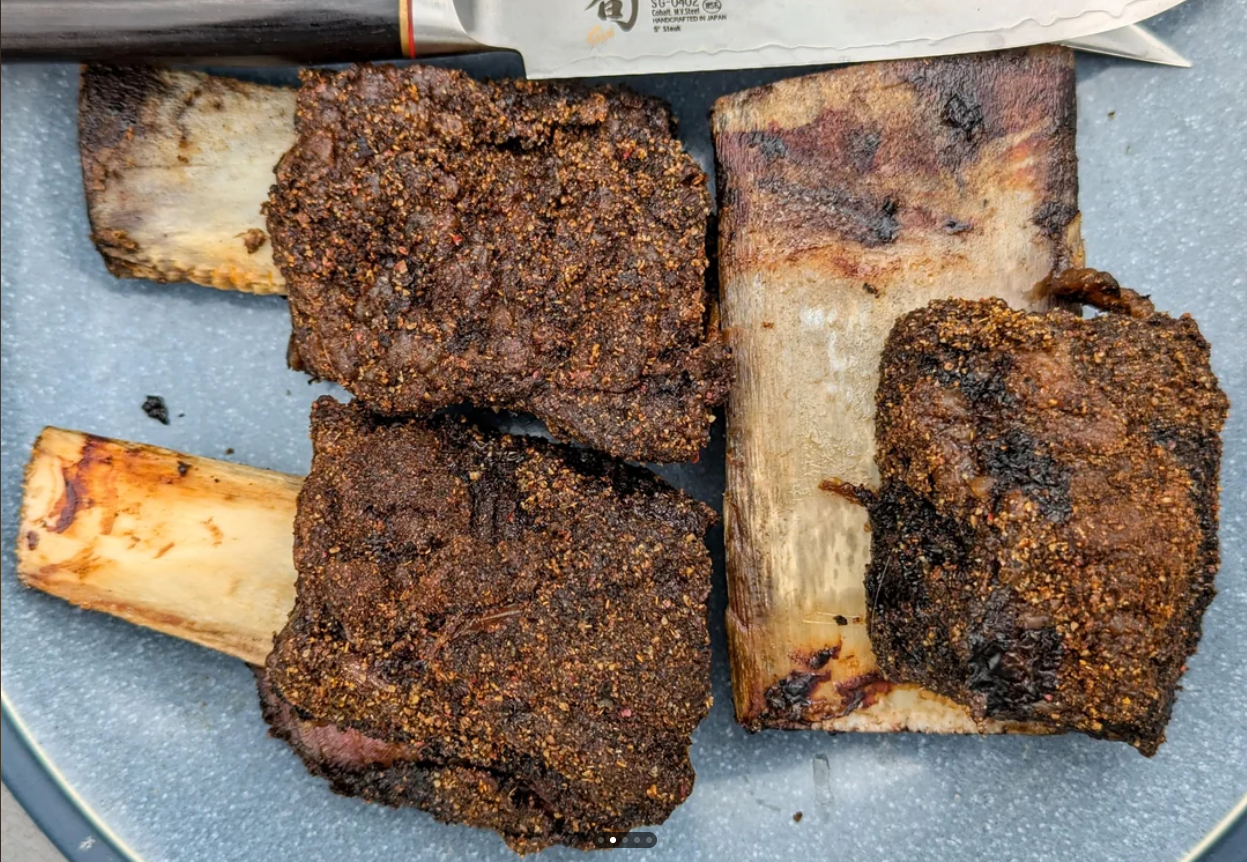 Four pieces of seasoned, cooked beef short ribs on a blue plate with a knife visible at the top.