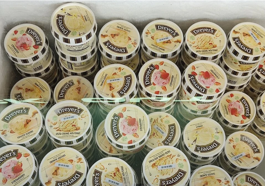 Tubs of Dreyer's ice cream in various flavors are stacked closely together in a freezer display at a store.