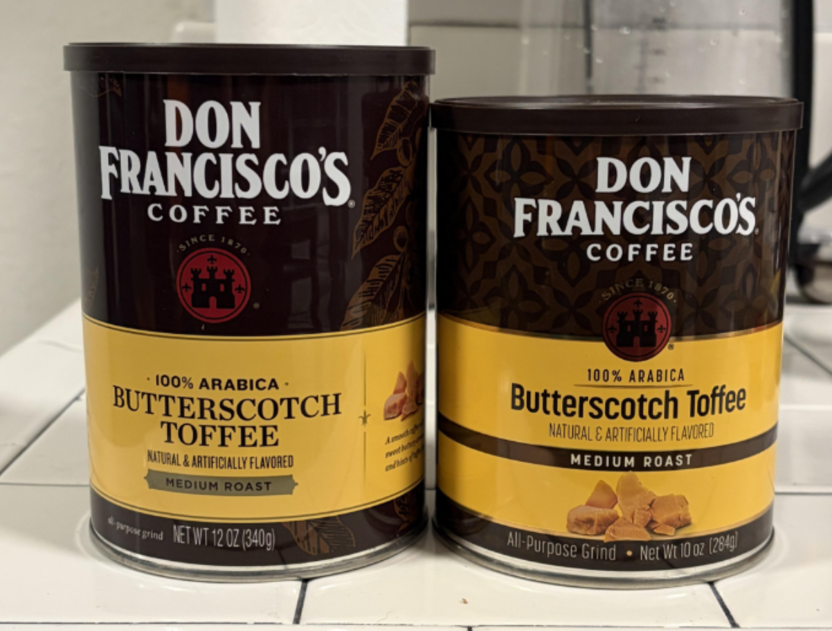 Two cans of Don Francisco's Coffee in Butterscotch Toffee flavor are side by side on a white tiled counter. The cans have brown labels with gold lettering and show pieces of toffee—a perfect example for those interested in photos of shrinking products, as these containers highlight changing packaging trends.