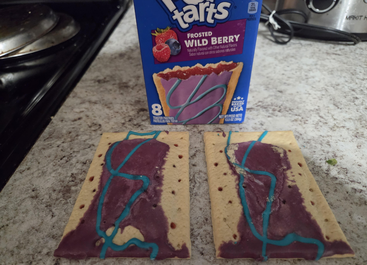 Two Frosted Wild Berry Pop-Tarts with purple icing and blue drizzle sit on a counter in front of their box, which shows an image of the same pastry—a classic scene often noted in photos of shrinking products.