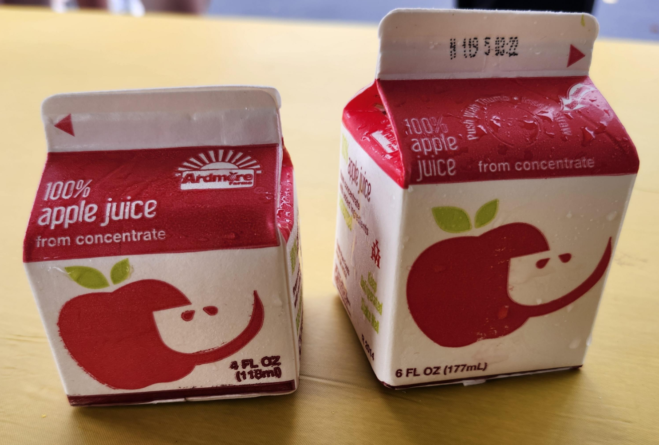 Two small cartons of Ardmore 100% apple juice from concentrate are on a yellow surface. Cartons are red and white, featuring a cartoon apple with a smiling face. These cartons may catch your eye if you’ve seen photos of shrinking products—a reminder of changing sizes over time.
